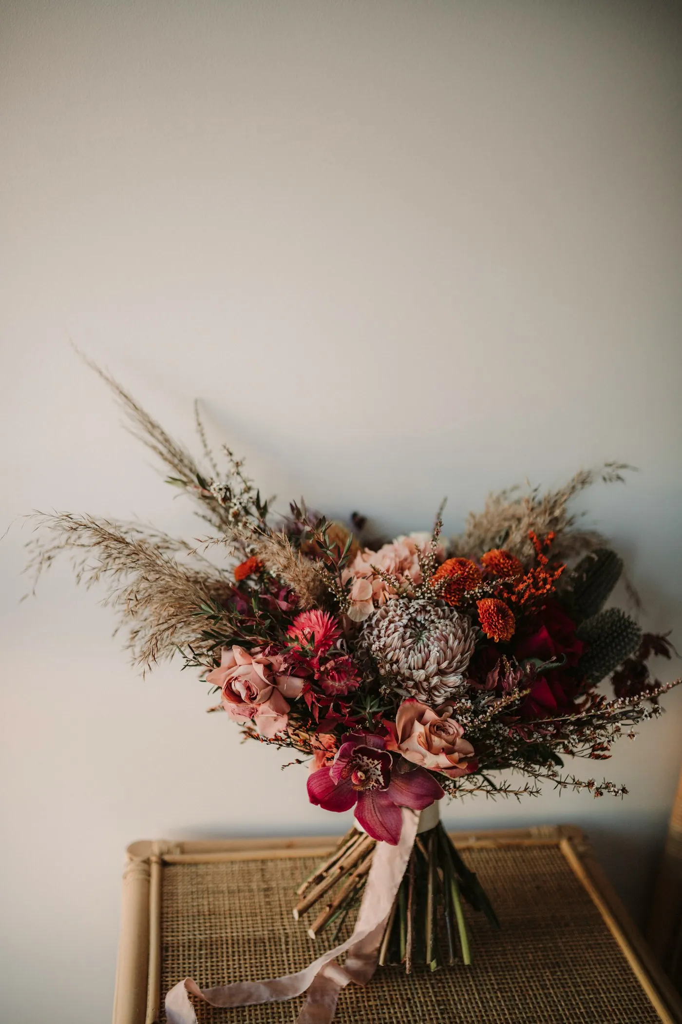 Textural hand-tied bouquet with roses, an orchid, and dried grasses.